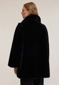 Czarny, pluszowy płaszcz z futerka syntetycznego z wysokim kołnierzem, opuszczanymi ramionami i luźną sylwetką. Charakteryzuje się gładką fakturą i czystymi liniami.