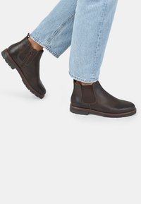 Stivali Chelsea in pelle marrone con pannelli elasticizzati laterali, punta arrotondata e suola in gomma testurizzata, abbinati a jeans cropped azzurri.