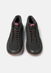 Black high-top shoes with a smooth texture, featuring a red "Camper" logo, brown laces, and a rubber sole with a slight curve.