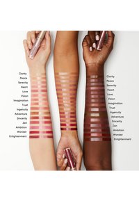 Läppprodukt med flera swatches på armar. Ljusa till mörka nyanser i varierande rosa och nude, som visar en glansig finish, märkta med namn.