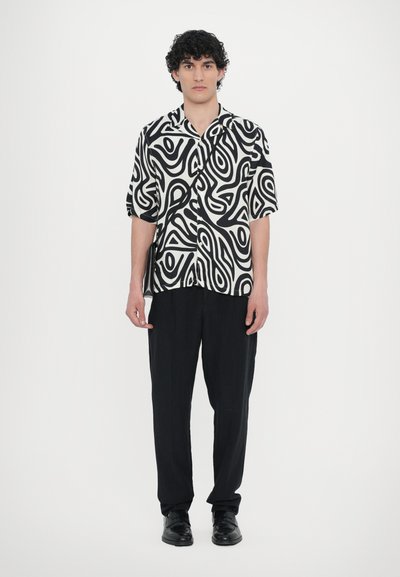 Short-sleeve shirt with a black and white abstract pattern, paired with black trousers and shoes. Smooth texture, relaxed fit.