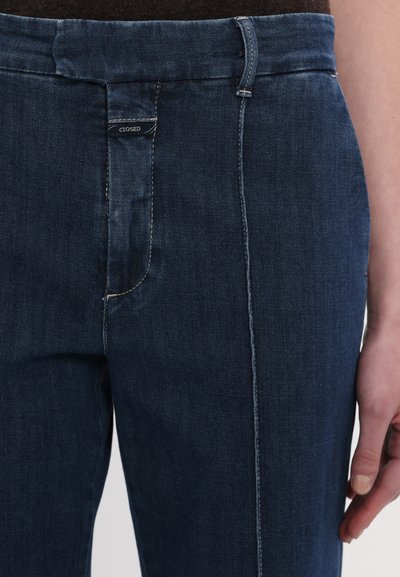 Granatowe dżinsy o prostym kroju, z kontrastowym przeszyciem i dyskretną metką marki na pasku. Gładka faktura i klasyczny design.