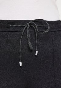 Black jogger pants feature a textured fabric, with a drawstring waistband in dark grey and white plastic tips. Includes side pockets.