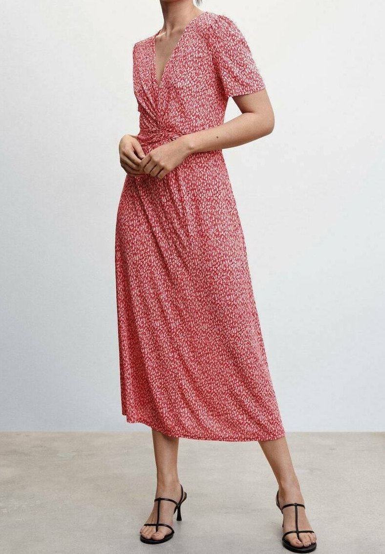 Rode bloemen wikkeljurk met korte mouwen, V-hals en geknoopte taille. Zachte stof met een vloeiende rok en een ontwerp tot op de enkel. Zwarte sandalen.