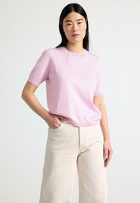 Pullover corto rosa chiaro a maniche corte realizzato in morbido materiale lavorato a maglia, con collo a giro e taglio morbido, abbinato a pantaloni a gamba larga color crema.