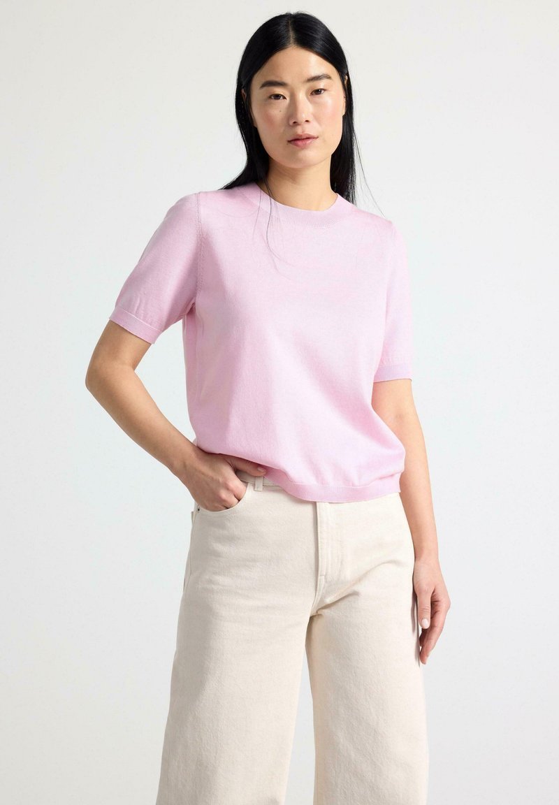Pullover corto rosa chiaro a maniche corte realizzato in morbido materiale lavorato a maglia, con collo a giro e taglio morbido, abbinato a pantaloni a gamba larga color crema.