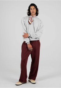 Felpa grigia, pantaloni bordeaux, sciarpa decorativa con motivo floreale. Design delle scarpe non coordinato: cappuccio beige, suola nera. Anelli d'argento alle mani.