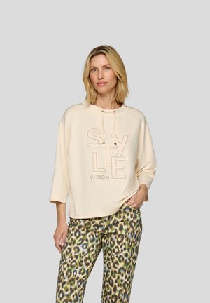 Helle beige Sweatshirt mit großem Drucktext "STYLE VISION", kombiniert mit grün- und braun-gefleckten Leopardenhosen.