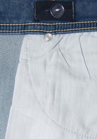 Tela de denim con un forro interior azul claro, que presenta un botón a presión plateado y costuras amarillas en contraste a lo largo del borde.