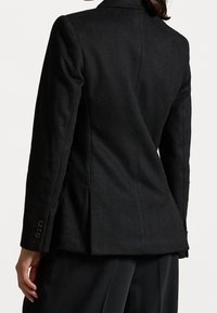 Svart skräddarsydd kavaj med lätt strukturerad yta, manschetter med en knapp och en figursydd form. Sidfickor och en kavajslag med hakar.