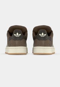 Paire de baskets Adidas marron avec semelles blanches, vue de dos montrant le logo trèfle de la marque sur la languette du talon.