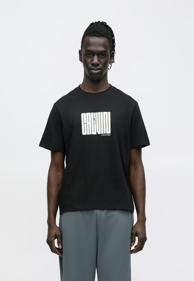 Μαύρο βαμβακερό μπλουζάκι με κοντά μανίκια και στρογγυλή λαιμόκοψη. Φέρει λευκό λογότυπο με το κείμενο «Calvin Klein» κεντραρισμένο.