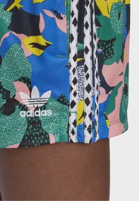Värikasta uimashortseja, joissa on eloisa kukkakuosi sinisen, vihreän, vaaleanpunaisen ja keltaisen sävyissä. Mukana valkoinen Adidas-logo ja raidalliset yksityiskohdat.