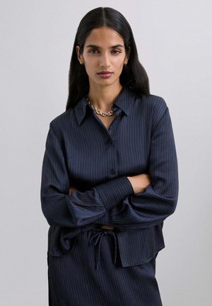 Camisa de botones a rayas azul marino con mangas largas y detalle de cintura atada, que presenta una textura suave y un corte relajado.