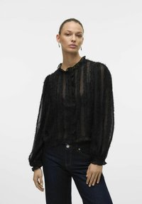 Must musta blouse volangidega ees, nööbiga kinnitus ja pikad puffvarrukad. Omab volangiga kaelaosa ja tekstuurilisi paneele. Sobib tumedate teksadega.