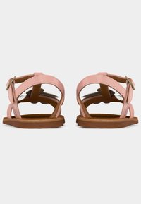 Sandales plates roses avec brides de cheville réglables et semelles marron, vues de dos sur un fond blanc.