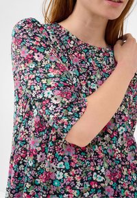 Blommig blus med korta puffärmar, rund halsringning och flerfärgade mönster på svart bakgrund, tillverkad av lättviktig tyg.