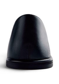 Chaussure en cuir noir avec un bout arrondi, une texture lisse et une semelle noire basse. Présente des coutures subtiles le long de l'arrière pour le détail.