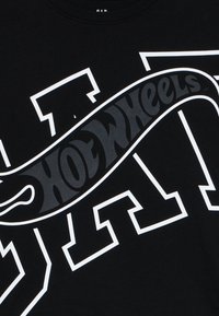 Schwarzes Baumwoll-T-Shirt mit einem großen weißen Grafiktext und einem gewölbten "Hot Wheels"-Logo in Schwarz mit glänzender Oberfläche.