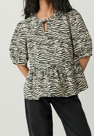 Personne portant un chemisier à imprimé zèbre noir et blanc avec des manches bouffantes et un col goutte d'eau, associé à un pantalon noir.