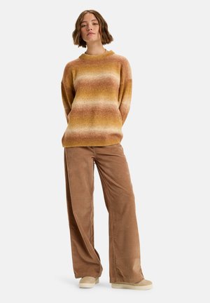Gebreide trui in oranje-geel verloop met een ronde hals, gecombineerd met beige corduroy wijde broekspijpen. Zachte textuur, casual pasvorm en zachte tinten.