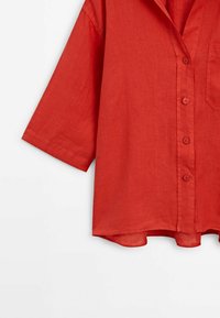 Chemise en lin rouge à manches courtes, col et poche avant. Avec des boutons sur le devant et un ourlet légèrement arrondi.