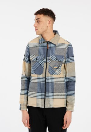 Fleece jacket with a blue and beige plaid pattern, featuring a zip closure, two chest pockets, and a classic collar. Textured fabric.