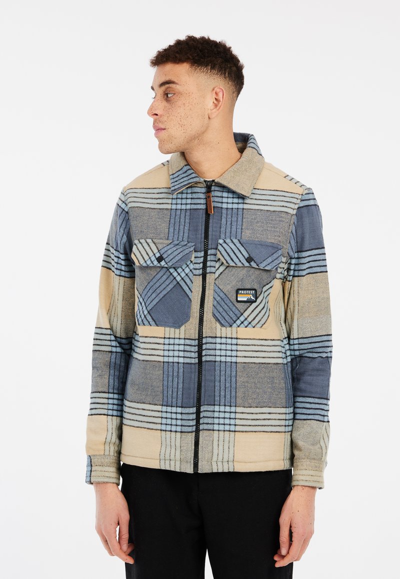 Veste en polaire avec un motif à carreaux bleu et beige, dotée d'une fermeture éclair, de deux poches poitrine et d'un col classique. Tissu texturé.