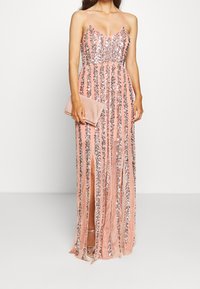 Rosa paljetterad maxiklänning med spagettiband, som har en hög slits på låret och vertikal randmönster. Matchad med en matchande clutch.