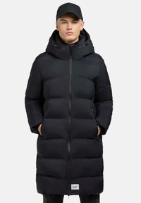 Piumino nero con zip full, cappuccio oversize e due tasche laterali. Presenta un design trapuntato e un piccolo logo sull'orlo.