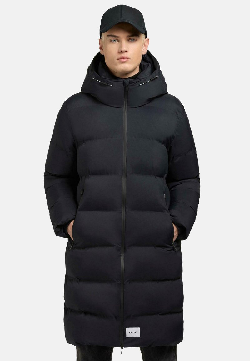 Piumino nero con zip full, cappuccio oversize e due tasche laterali. Presenta un design trapuntato e un piccolo logo sull'orlo.