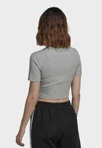 Grå bomullskortärmad t-shirt med rund halsringning, kombinerad med svarta byxor med elastisk midja och sidostråkar.