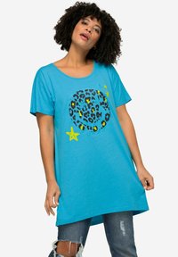 Camiseta de manga corta turquesa con un diseño de círculo de estampado de leopardo y acentos amarillos y estrellas. Tejido suave, corte relajado y espalda más larga.