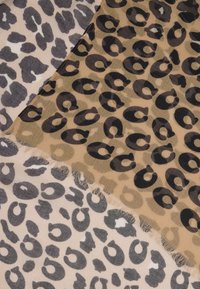 Tkanina s leopardím vzorom v odtieňoch šedej a pieskovej. Materiál zobrazuje rôzne vzory so zaschnutými okrajmi a jemným, textúrovaným povrchom.