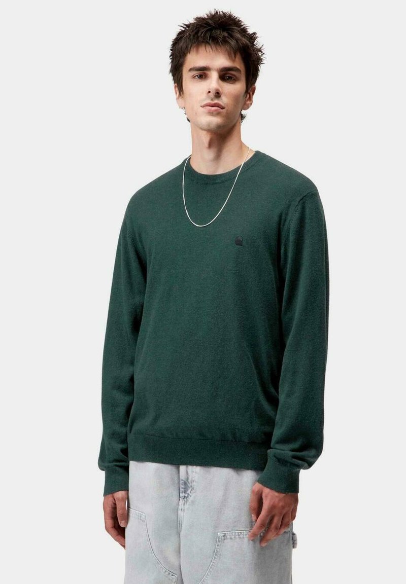 Jersey verde de cuello redondo hecho de una tela suave, con mangas largas y un dobladillo ajustado. Presenta un pequeño logo negro en el pecho.