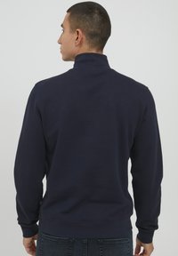 Tricou bleumarin cu un guler înalt, cu manșete și un tiv ribbat. Creat dintr-un amestec de bumbac, evidențiind o textură netedă și un design solid.
