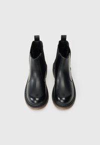 Bottines en cuir noir avec des panneaux élastiques sur les côtés, semelles en caoutchouc plates et languettes pour un enfilage facile. Texture lisse et design épuré.
