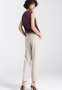 Bezramienna burgundowa bluzka zestawiona z beżowymi spodniami na elastycznej talii. Spodnie mają boczne kieszenie, a model nosi brązowe sandały na obcasie.