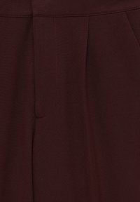 Tissu brun foncé en gros plan montrant des coutures sur mesure et des plis, probablement partie d’un vêtement comme un pantalon ou une jupe.