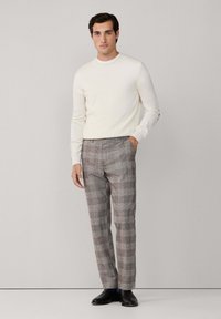 Cremiger Pullover und graue karierte Hose, aus einem strukturierten Stoff und mit tailliertem Schnitt, kombiniert mit schwarzen Schuhen. Einfaches Design und neutrale Farben.