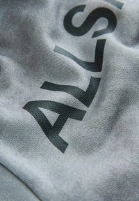 Šedá látka s jemnou texturou, na které je velký černý text. Materiál vypadá lehký s hladkým, mírně lesklým povrchem.