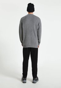 Suéter gris de punto con una textura acanalada, mangas largas y cuello redondeado, combinado con pantalones de pana negros y zapatillas gris.