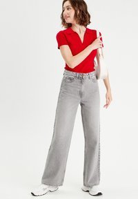 Camisa polo roja con cuello, combinada con jeans grises de pierna ancha y cintura alta. Zapatillas blancas complementan el look, junto con un pequeño bolso.