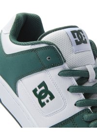 Green and white sneakers with leather and mesh materials. Features a padded collar, lace-up front, and a green logo on the side.