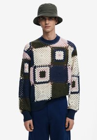 Strickpullover mit einem mehrfarbigen Patchwork-Design in Tönen von Marineblau, Grün, Pink und Creme. Er hat einen gerippten Rundhalsausschnitt und Bündchen.