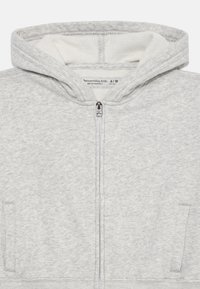 Sweat à capuche gris zippé avec intérieur en polaire, comprenant une capuche réglable, deux poches latérales et un ourlet côtelé. L'étiquette indique la taille 9/10.