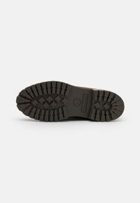 Sole de cizme din cauciuc negru, cu șanțuri adânci pentru aderență. Prezintă un logo central și o combinație de modele ridicate și plate.