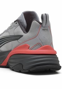 Chaussure de sport grise avec une tige texturée, des accents noirs, une semelle intermédiaire rose prononcée et une languette à l'arrière pour un enfilage facile.