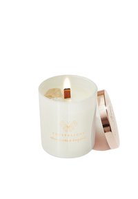 Biała szklana świeca z drewnianym knotem, zawierająca wewnątrz kryształ przezroczystego kwarcu. Metaliczna przykrywka w kolorze różowego złota oraz etykieta dodają delikatnego akcentu.