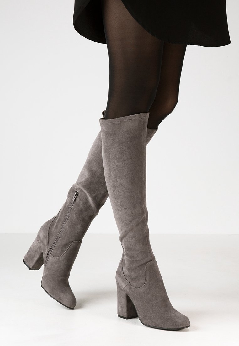 Stivaletti grigi in suede sopra il ginocchio con tacco a blocco, caratterizzati da un design elegante e una cerniera laterale per una facile vestibilità. La texture liscia accentua l'aspetto.